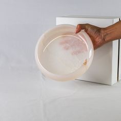 a hand is holding a plastic bowl in front of a white box on the floor