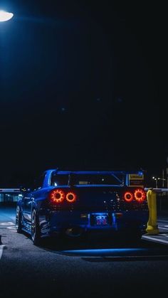 the back end of a blue car parked in a parking lot at night with its lights on