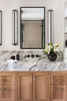 a bathroom with marble counter tops and wooden cabinets, along with two black vases filled with flowers