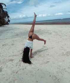 a woman doing a handstand on the beach with palm trees in the background