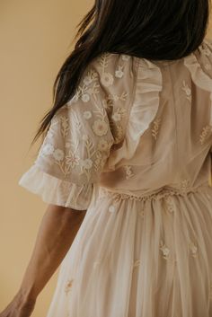 the back of a woman's dress with white flowers on it and ruffled sleeves