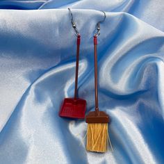 two red and yellow broom shaped earrings on a blue satin background with silver earwires