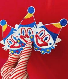 a hand holding two clown masks on top of each other in front of a red background