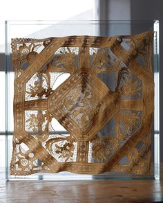 an intricately designed piece of art in a glass case on a wooden table next to a window