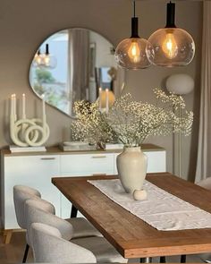 a wooden table topped with a vase filled with flowers next to two lights hanging from the ceiling