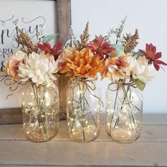 three mason jars filled with flowers and fairy lights on a wooden table next to a framed sign