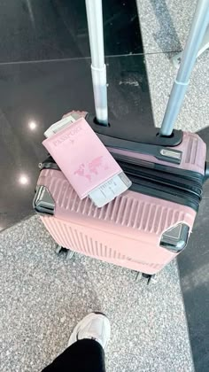 a pink piece of luggage sitting on top of a floor next to a person's feet