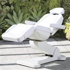 a white reclining chair sitting on top of a cement floor in front of plants