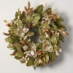 a wreath with white flowers and green leaves is hanging on the wall next to a candle