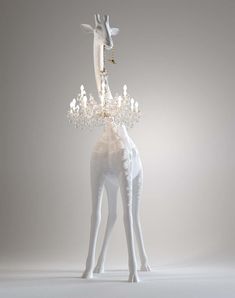 a white giraffe with a chandelier on its neck and legs, standing in front of a gray background