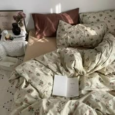 an unmade bed with sheets, pillows and a book on the floor next to it