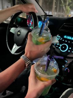 two people holding drinks in their hands while sitting in a car with steering wheel controls