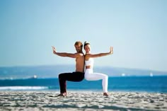 a man and woman doing yoga on the beach