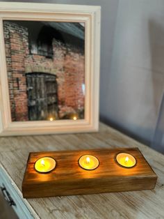 three lit candles sitting on top of a wooden table next to a framed photo and candle holder