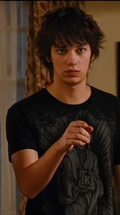 the young man is wearing a black t - shirt and holding his hands together in front of him