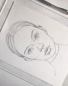 a pencil drawing of a woman's face on a piece of paper next to a pen