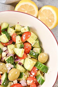 a white bowl filled with cucumber, tomatoes and other vegetables next to sliced lemons