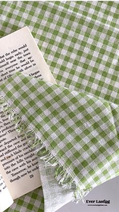 an open book laying on top of a green and white checkered table cloth next to a piece of paper