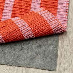 an orange and white checkered rug laying on top of a wooden floor next to a gray mat