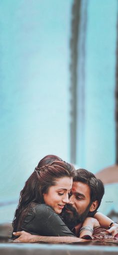 a man and woman laying on the ground in front of some water with their arms around each other