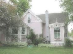 a pink house with white trim on the front and side of it, surrounded by trees