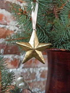 a gold star ornament hanging from a christmas tree in front of a brick wall