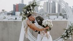 a bride and groom kissing in front of a circular arch with greenery on it