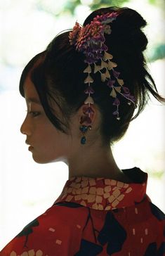 a woman with flowers in her hair wearing a red and black kimono, looking off to the side