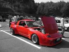 a red sports car parked in a parking lot with its hood open and people looking at it