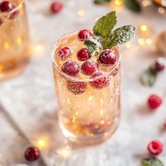 two glasses filled with ice and cranberries on top of a white tablecloth