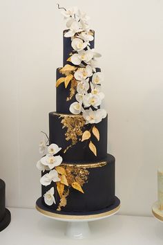 a three tiered black and gold wedding cake with white orchids on the side