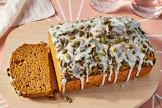 a loaf of pumpkin bread with white icing and pumpkin seeds on top, sitting on a wooden platter