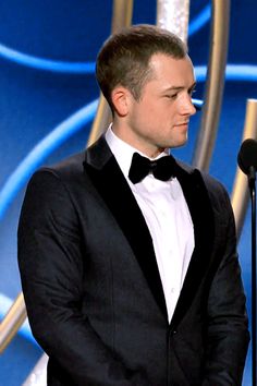 a man in a tuxedo standing next to a microphone