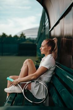 a woman sitting on top of a green bench holding a tennis racquet