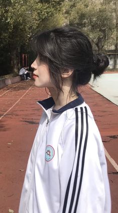 a woman with black hair standing in front of a tennis court wearing a white jacket