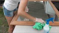 a woman is cleaning a mirror with a spray bottle and cloth on the table next to it