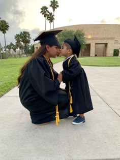 a woman kneeling down next to a little boy wearing a graduation cap and gown on