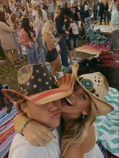 two women in cowboy hats at an outdoor music festival, one is hugging the other