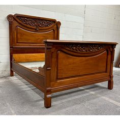 a wooden bed frame with intricate carvings on the headboard and foot board is shown in front of a white brick wall