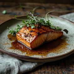 a piece of salmon on a plate with sauce and garnished greens, ready to be eaten