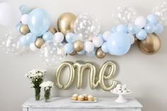 a table with balloons, cake and cupcakes on it in front of a one sign