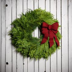 a green wreath with a red bow hanging on a white wooden wall next to wood planks