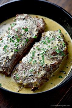 two pieces of meat in a skillet on a wooden table with green garnishes