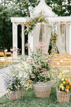 several baskets filled with flowers sitting on top of a grass covered field next to a white gazebo