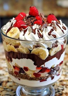 a dessert in a glass dish with chocolate, banana and raspberries on top