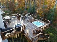 a hot tub sitting on top of a wooden deck next to a wooded area with tables and chairs