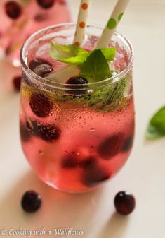 two glasses filled with liquid and strawberries on top of a white table next to green leaves