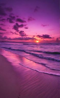 the sun is setting over the ocean with waves coming in to shore and footprints on the sand