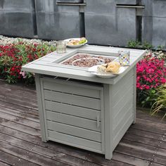 an outdoor table with food and drinks on it in front of some pink flowered bushes