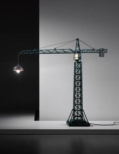 a green crane lamp sitting on top of a white table next to a black wall